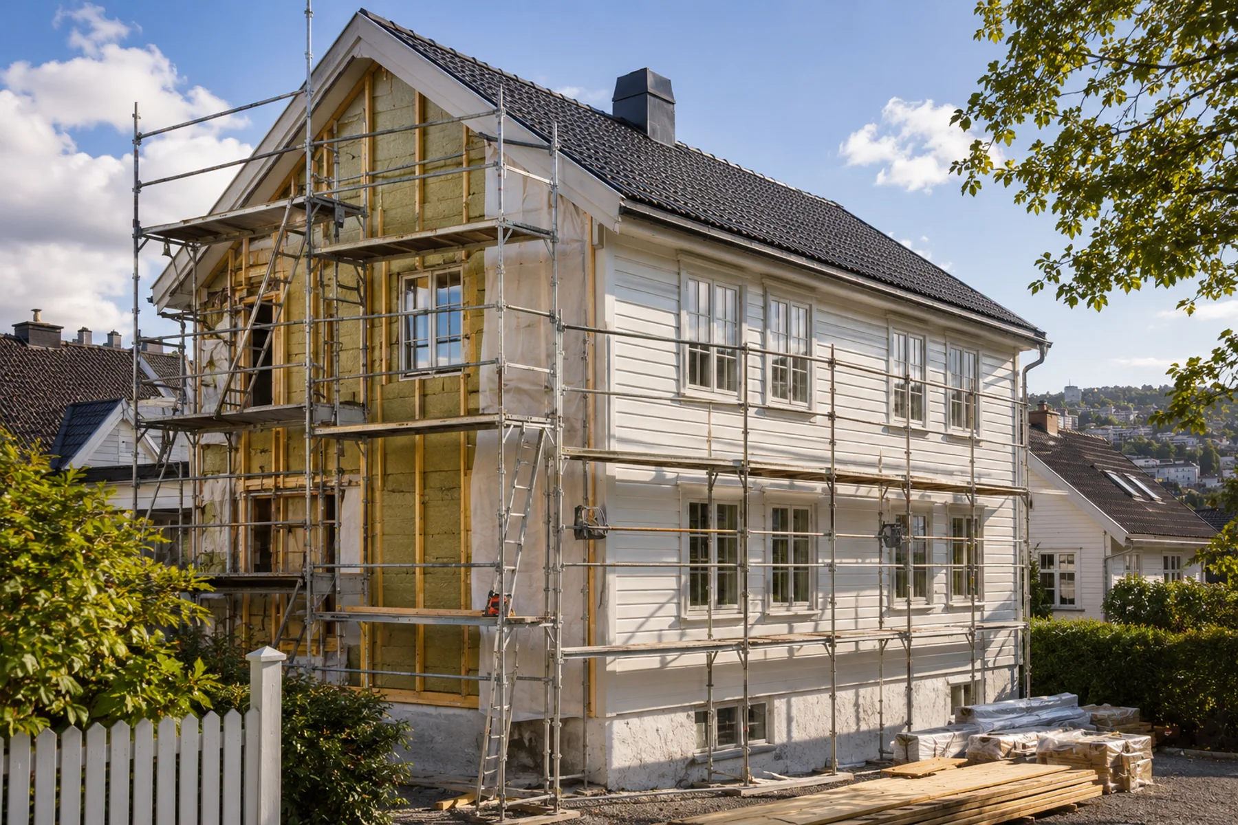 Klassisk hvitt trehus med stillas, åpen gavl, isolasjon og delvis ferdig kledning