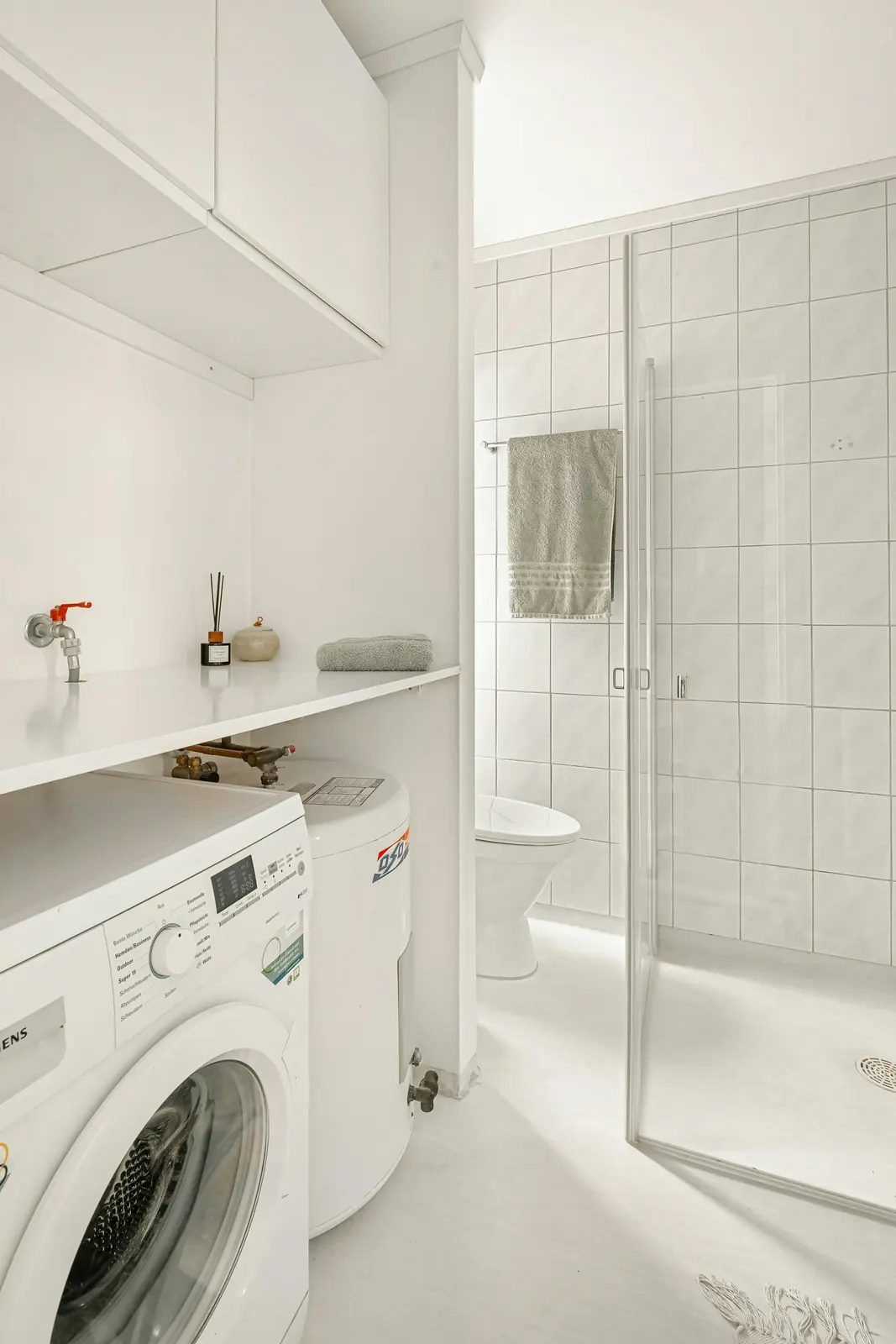 Lite vaskerom med vaskemaskin, dusjsone, fliser og våtromsflater