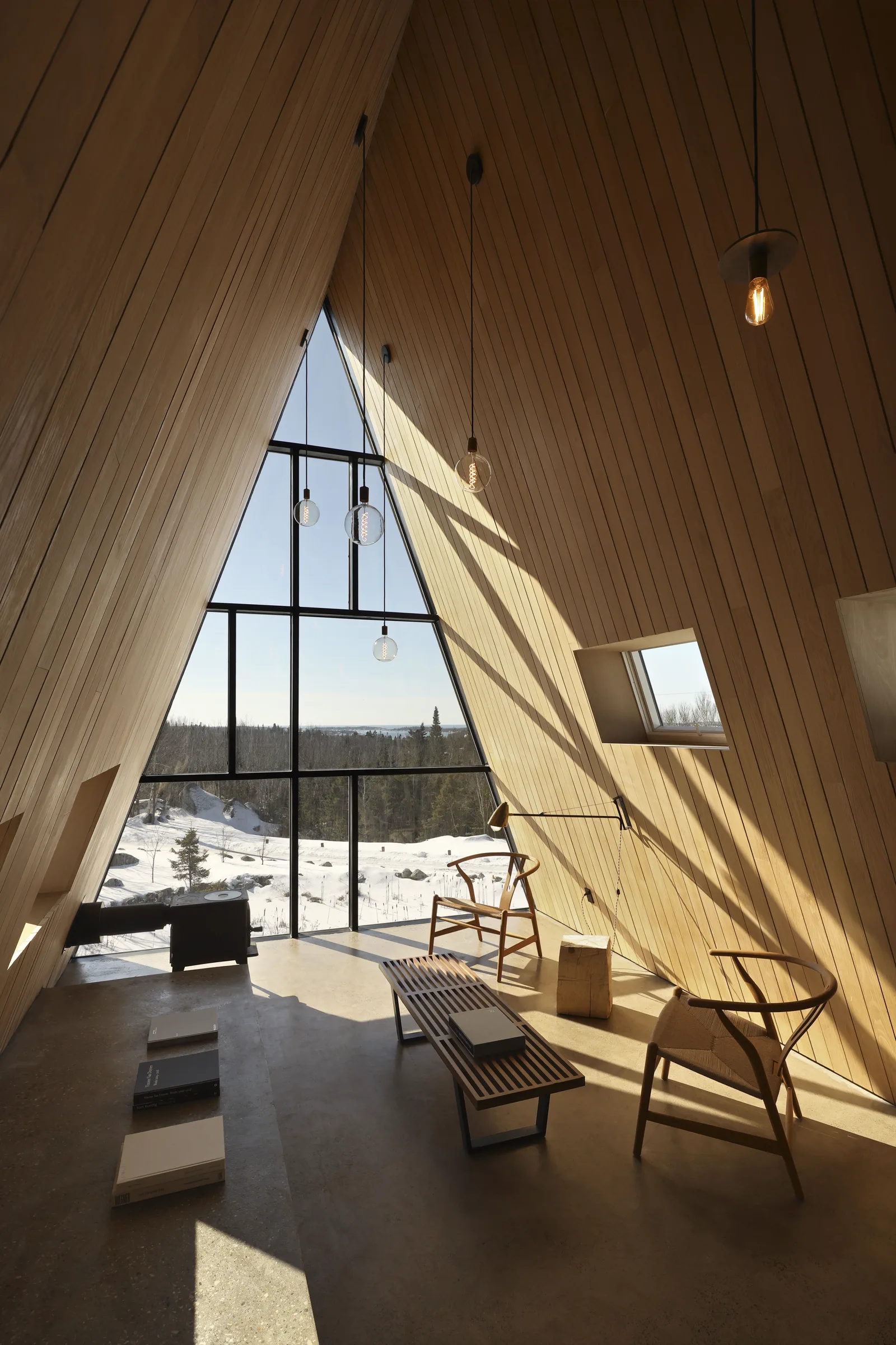 Oppholdsrom i A-hytte med store glassfelt, lenestoler, trehimling og vinterlys