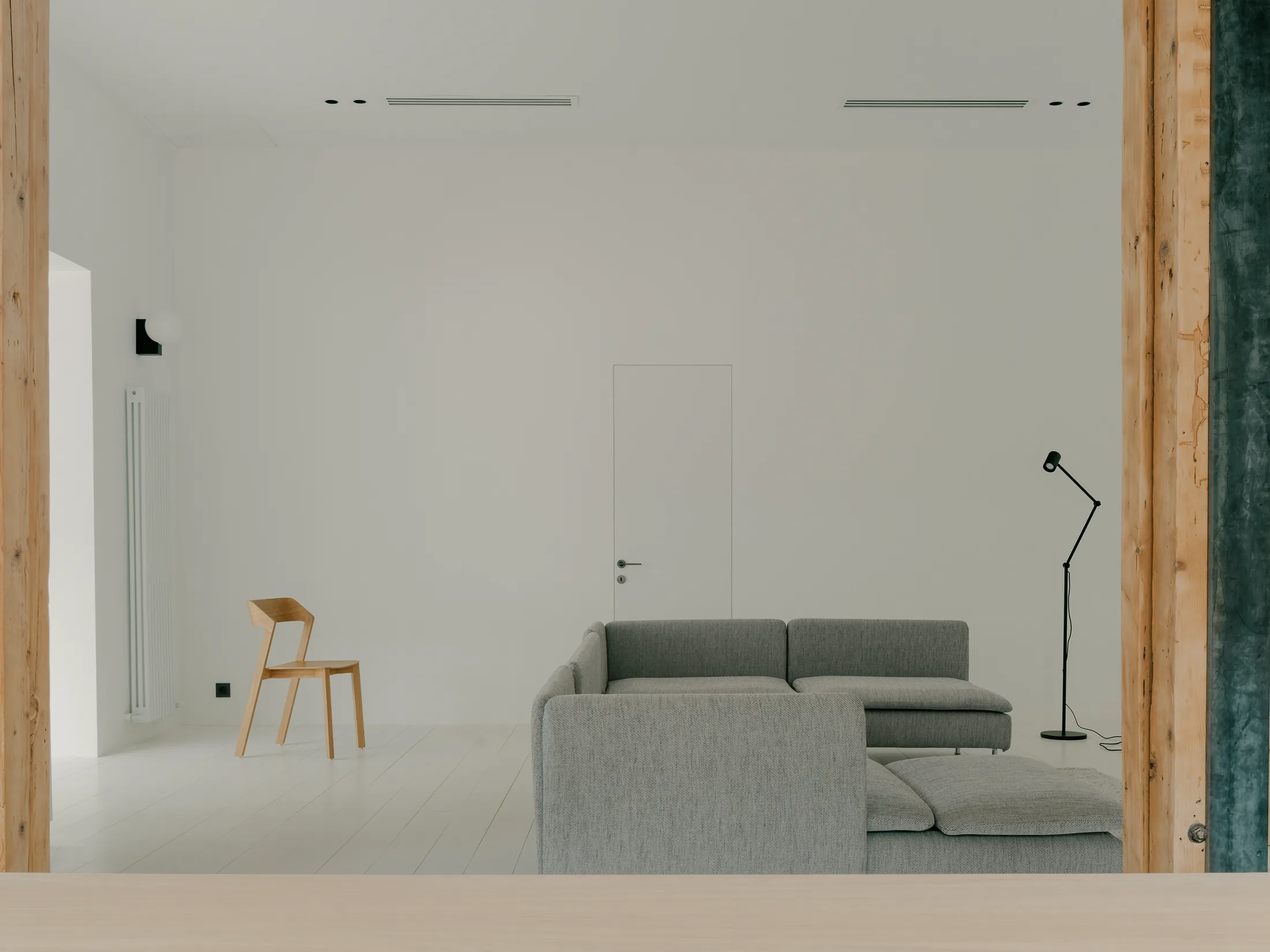 Stue med sofa, stol, synlige trestolper og hvite gulv