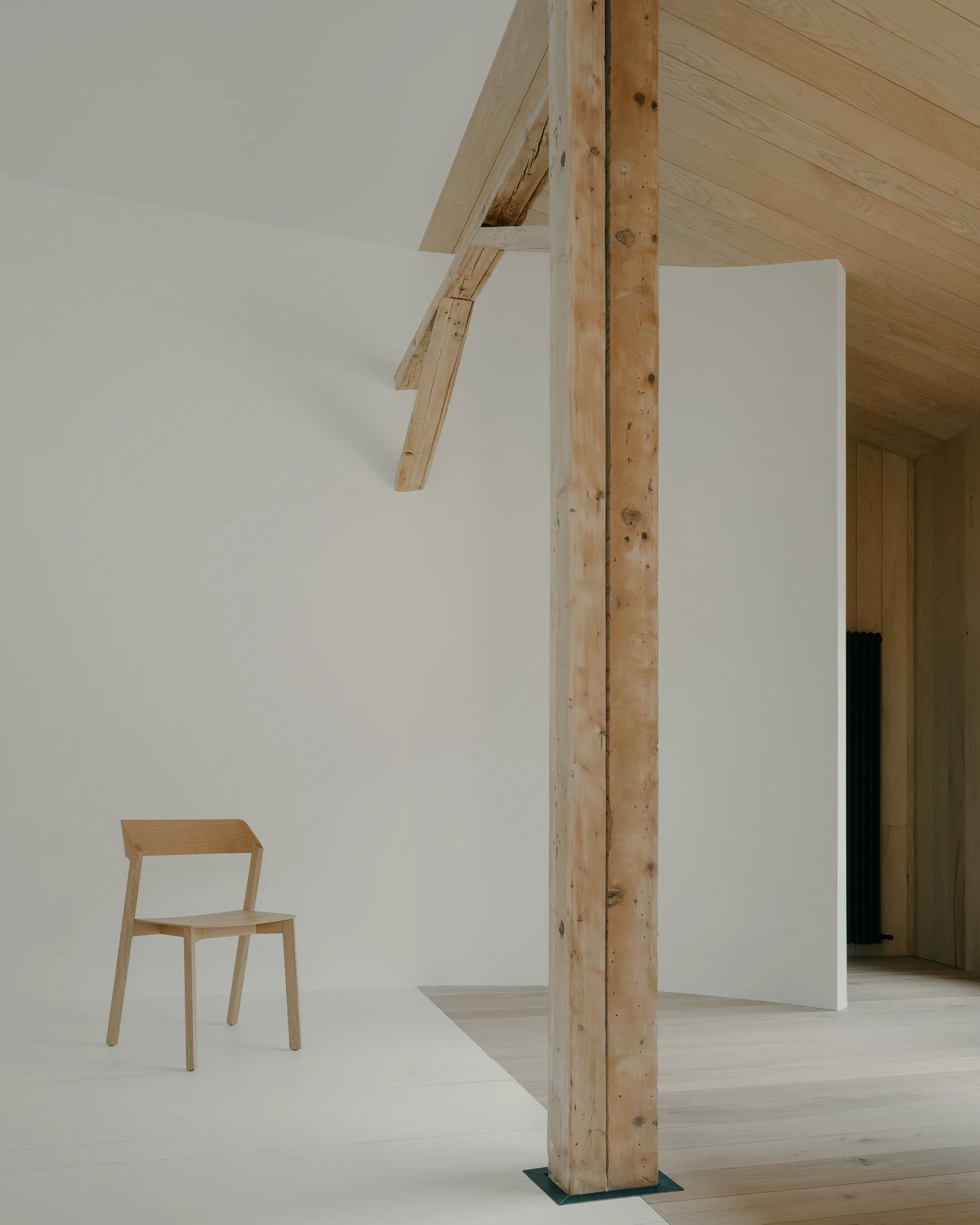 Lyst rom med stolpe, trehimling og enkel stol